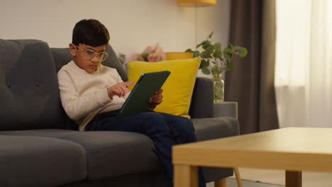 Young-Boy-Sitting-On-Sofa-At-Home-Playing-Games-Or-Streaming-Onto-Digital-Tablet-8